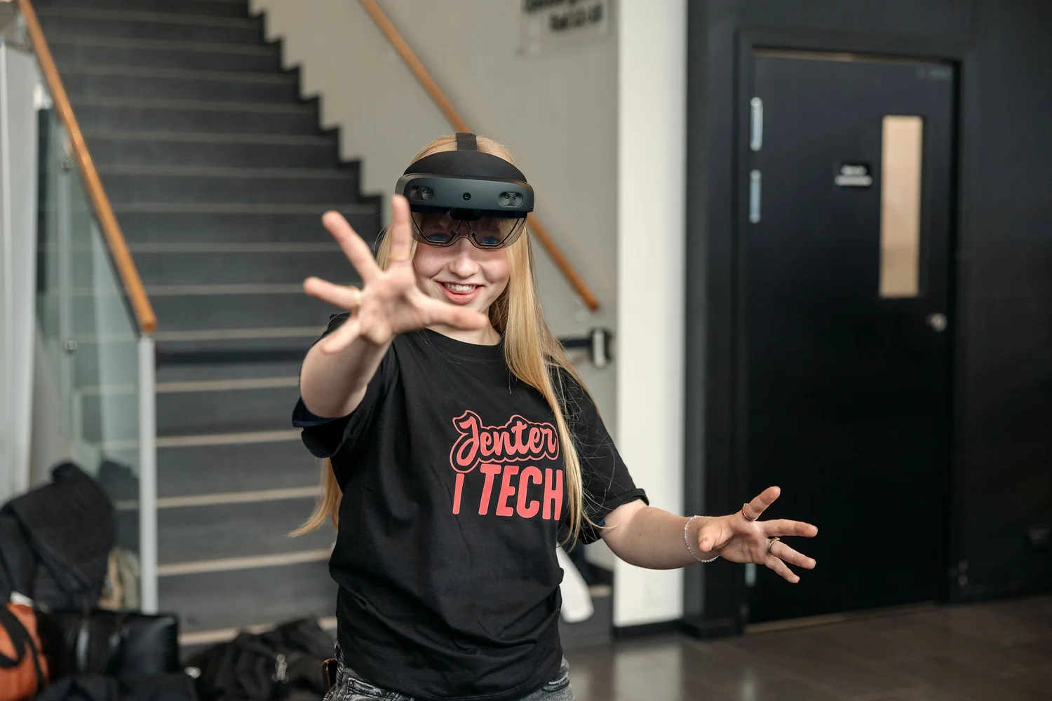 Jente i Jenter i Tech-t-skjorte prøver eit par blanda røyndom-briller og strekkjer handa mot noko berre ho ser